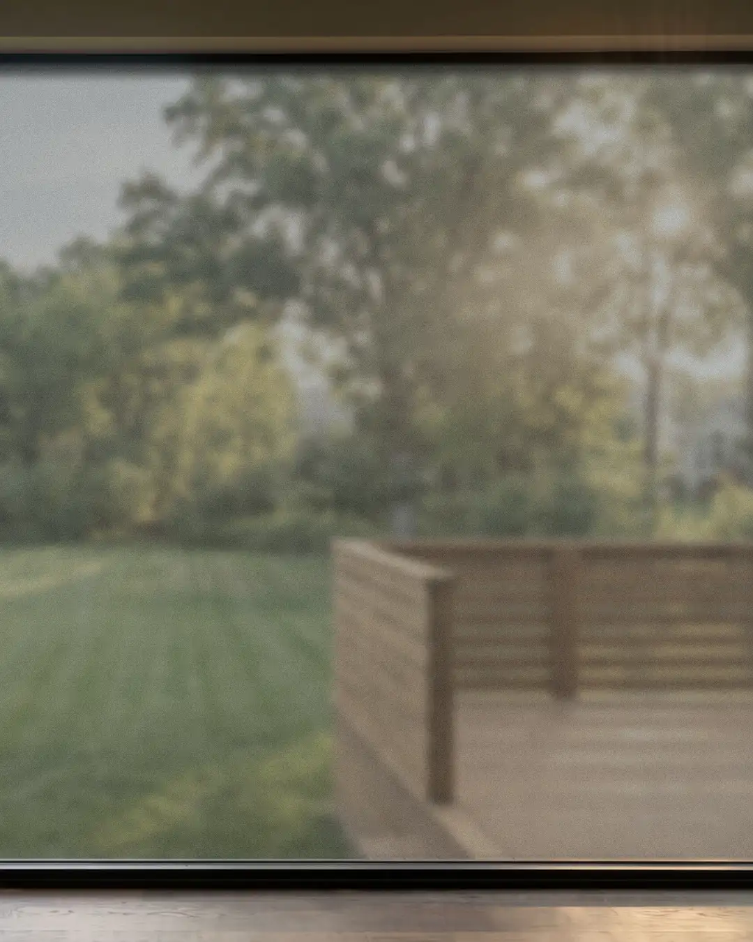 View through a fogged window: sunlit backyard with trees and a wooden deck