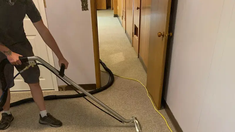 Hot-water extraction cleaning a carpeted corridor, the wand mid-pass