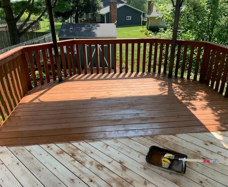 A deck half-stained — fresh color across the finished boards, bare wood still ahead of the stain tray