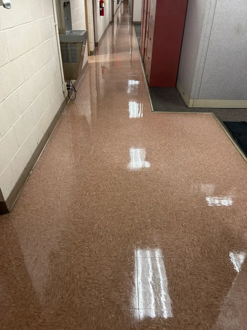 A commercial VCT corridor re-coated to a high-gloss finish that mirrors the ceiling lights