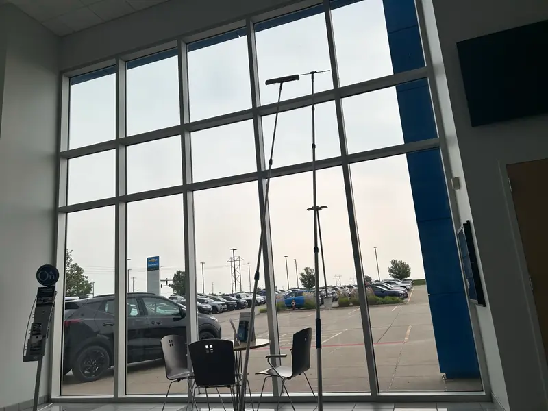 A water-fed pole cleaning the outside of a commercial showroom's two-storey window wall, seen from the lobby